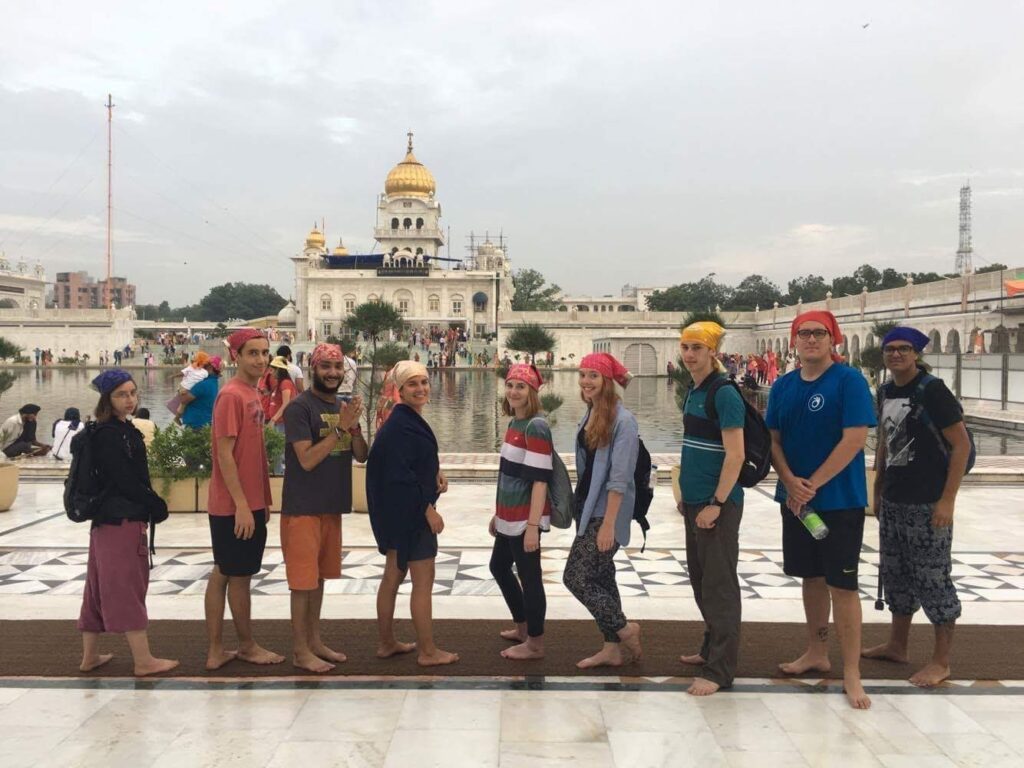 Nine people standing in front of a body of water and a temple in India