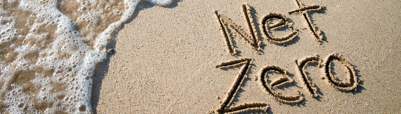 'Net zero' written in the sand on a beach