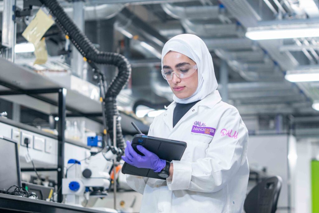 A student wearing PPE imputing data into a tablet computer