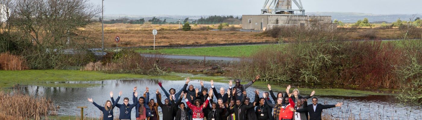 group of people waving in front of a radio telescope