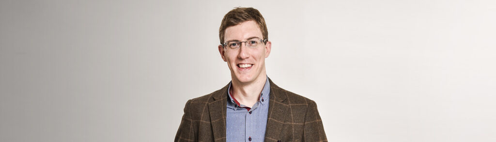 Smiling man in glasses in front of a plain background