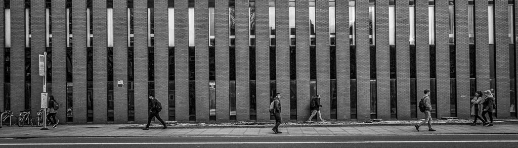 Black and white photo of people in distance walking along a road by a university building