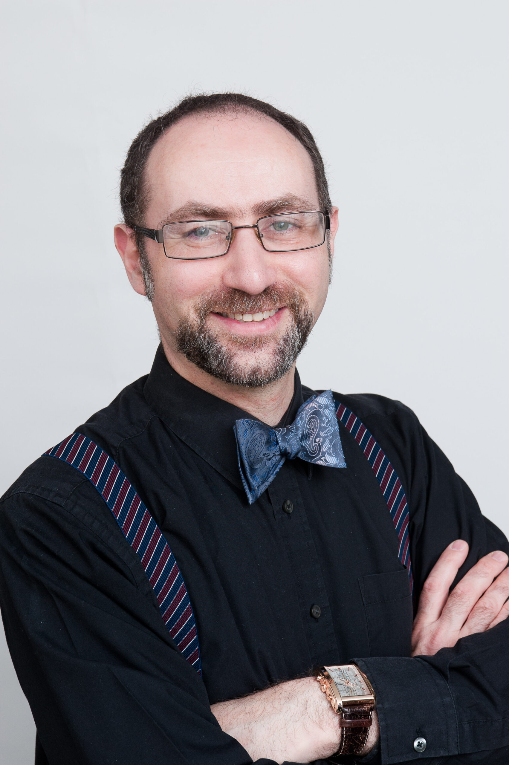 Bearded man in glasses, wearing black shirt, bow tie and braces
