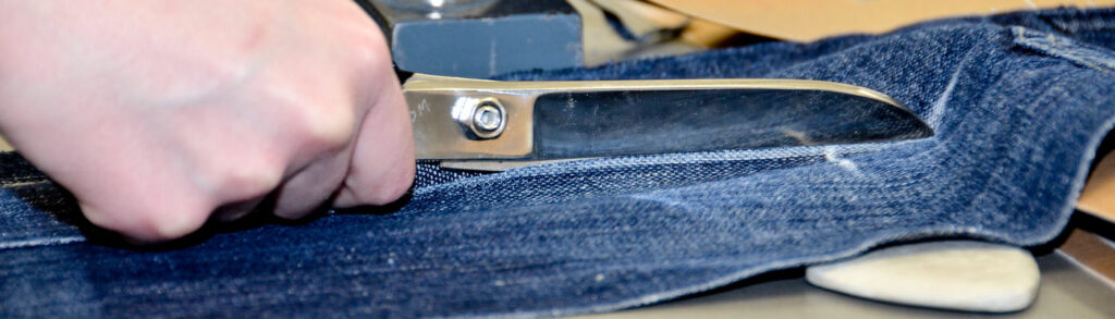 Close up of a hand and scissors, cutting denim