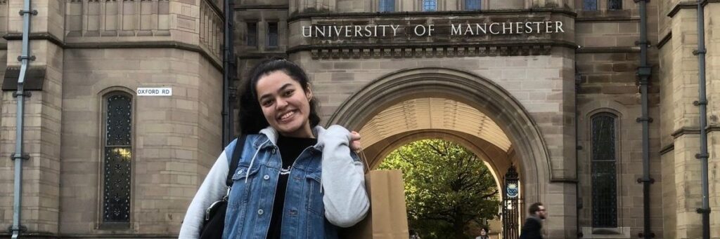 Woman in front of main Manchester University entrance sign