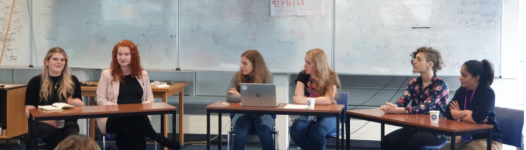 Six people sitting in a semicircle behind tables