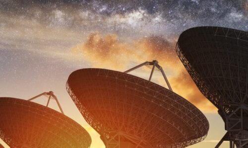 A row of satellite dishes pointing up to the night sky.