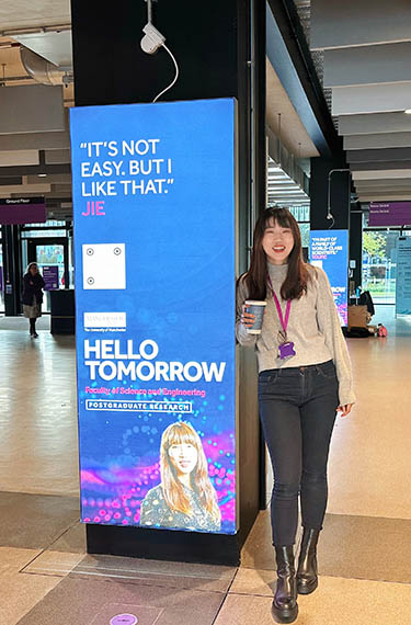 Jie Wang leaning against a display in the foyer of the MECD building
