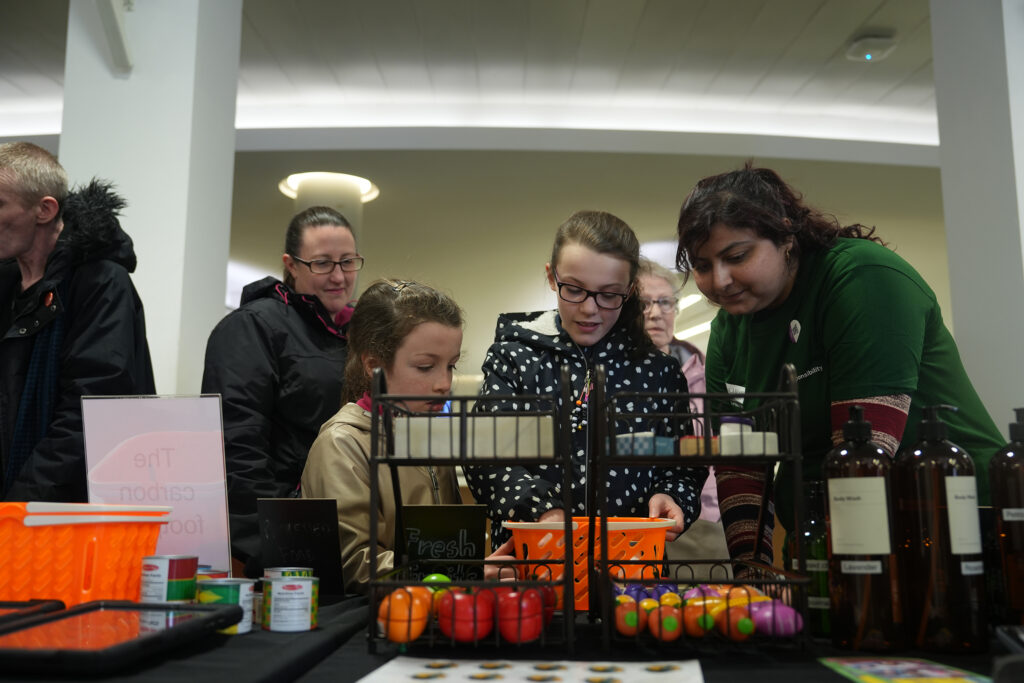 Three children and a student volunteer calculating their carbon footprint using toy fruit and vegetables. 