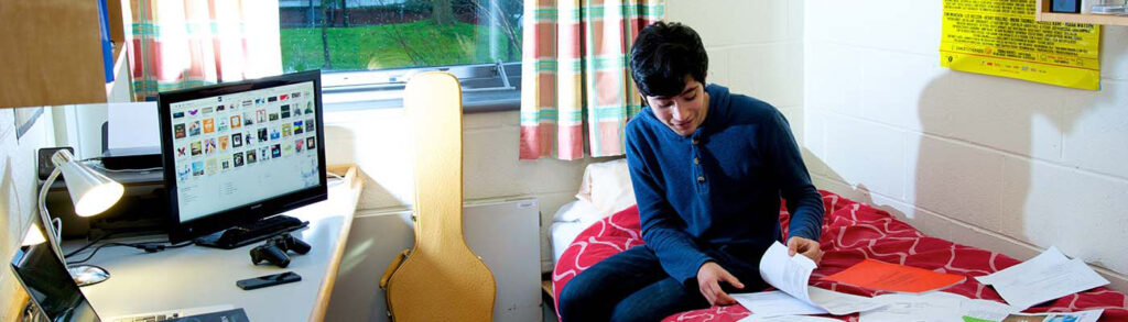 A student sitting on a bed in a room in halls of residence