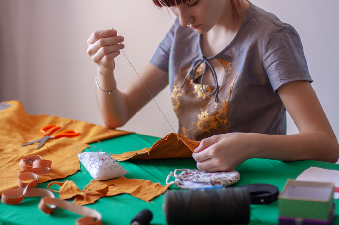 Person sewing clothes surrounded by sewing equipment