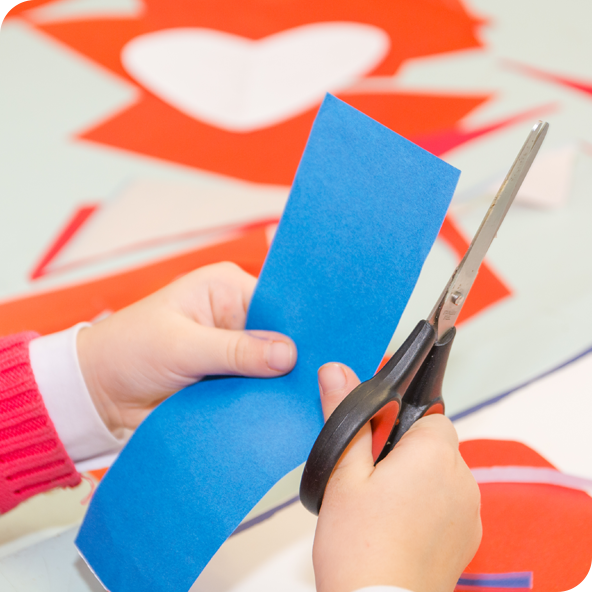 Hands holding a pair of scissors cutting shapes out of colourful paper