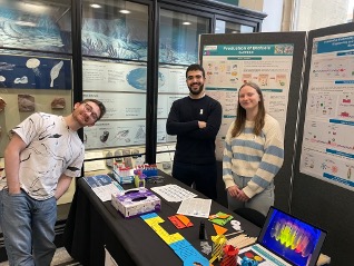 Three volunteers stood smiling beside their stall table and posters